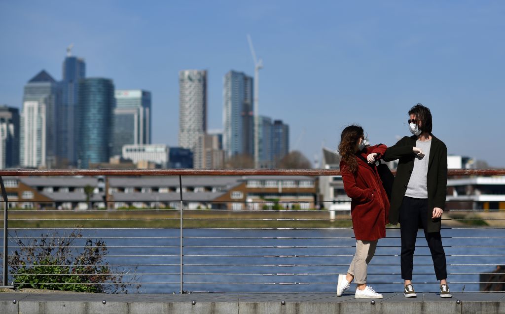 People wearing face masks as a precautionary measure against covid-19 'elbow bump' as they stand in Greenwich in south London