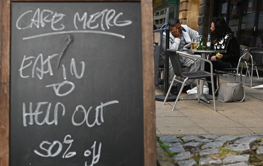 Diners sit at table near a sign promoting the British government's "Eat out to Help out" scheme
