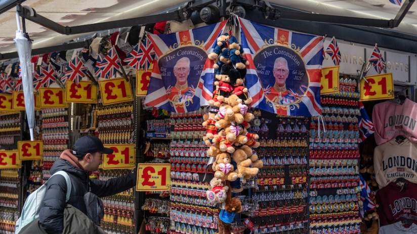 LONDON, ENGLAND - APRIL 24: A man looks at items on display at a souvenir stand as King Charles III Coronation flags are displayed above him on April 24, 2023 in London, England. The Coronation of King Charles III and The Queen Consort will take place on May 6, part of a three-day celebration. (Photo by Carl Court/Getty Images)