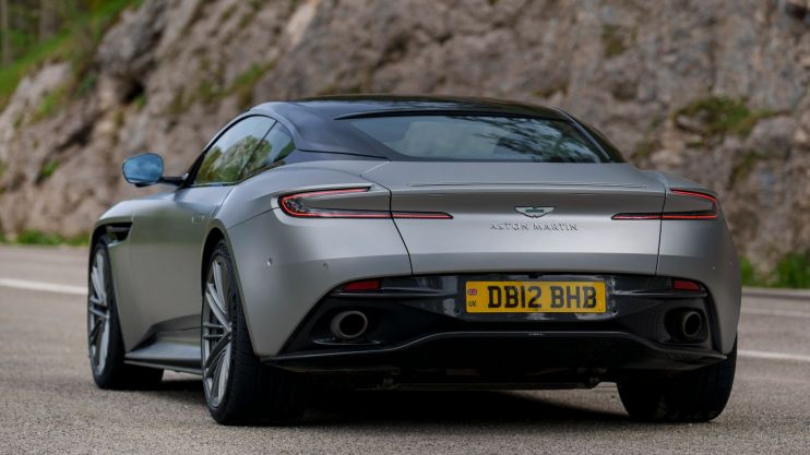 Aston Martin losses halved in its full-year results despite a hit to wholesale volumes after production issues with the roll-out of its DB12 model.