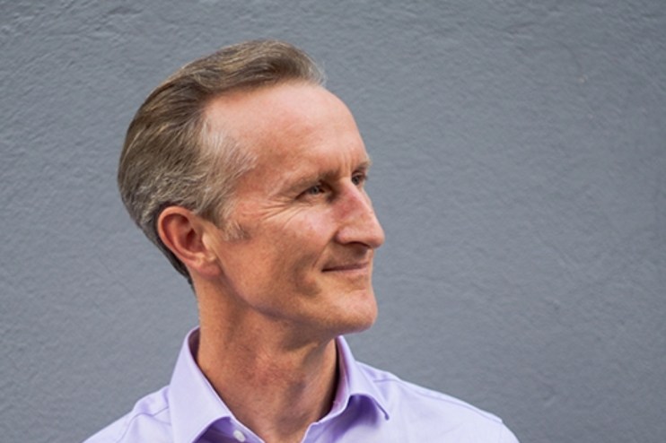 Image of a man in a purple collared shirt looking to his left