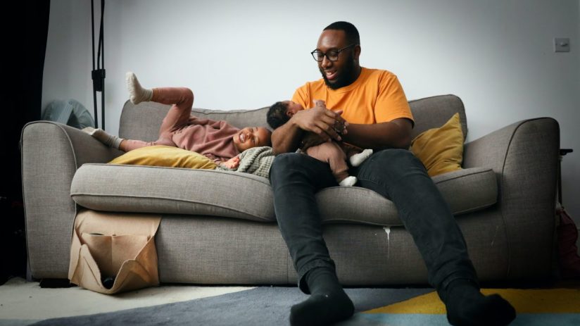 LONDON, ENGLAND - FEBRUARY 14: Aaron Jaunty, 38, sits for a portrait with his daughter, Zora, and newborn son, Elias, at their home in Chingford on February 14, 2024 in London, England. Aaron says "Being a Black Dad means love and patience, trial and improvement. Alignment with my wife, my family, my village. Possibility". Dope Black Dads was formed by Marvyn Harrison on Father's Day 2018, first as a WhatsApp group of with 23 Black fathers he knew in London. It has since developed as a digital safe space for some 40,000 fathers from the international community to discuss their experiences of being black, a parent and masculinity in the modern world. It brings together men navigating fatherhood, societal pressures and the age-old stereotype of the absent Black father. Far too often societal biases perpetuate the myth of absent or disengaged lack fathers, the photographer sees this portrait series as an opportunity to uplift the ideology of Black men, especially in their role as fathers. A body of work that celebrates joy, pride and love. These portraits serve as a tribute to Black families' strength, resilience and beauty, amplifying their voices and contributing to a more nuanced and compassionate understanding of Black fatherhood. (Photo by Alishia Abodunde/Getty Images)