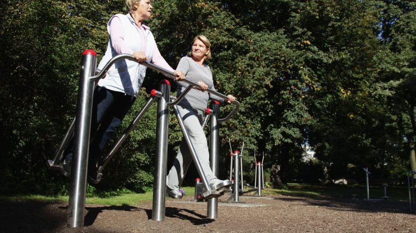 Two older women exercising at an outdoor gym in sunshine