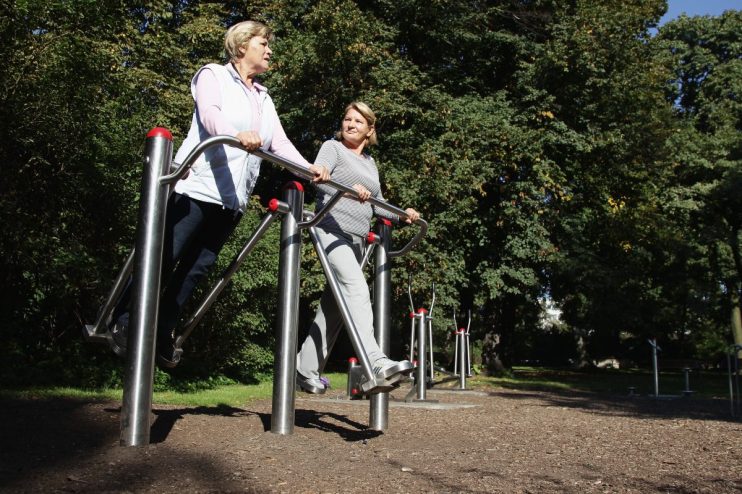 Two older women exercising at an outdoor gym in sunshine