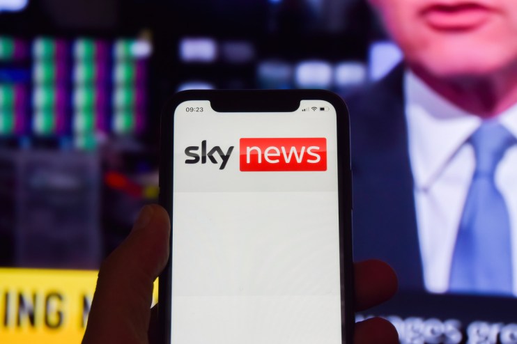 Sky News logo on a phone in front of a broadcast from the news channel