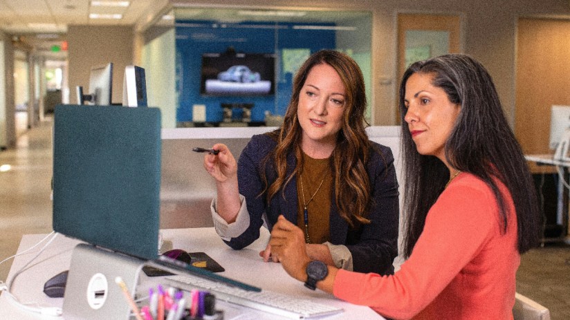 Two business women talking about sales in office at desk with laptop (Photo: Unsplash)